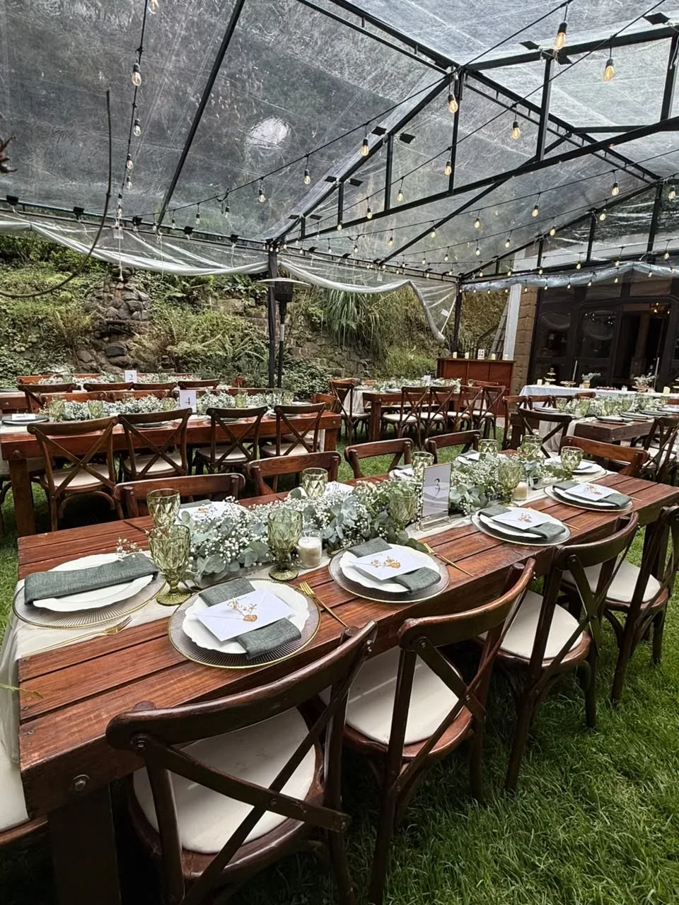 Boda en jardín con mesas largas de madera, copas verdes y servilletas salvia